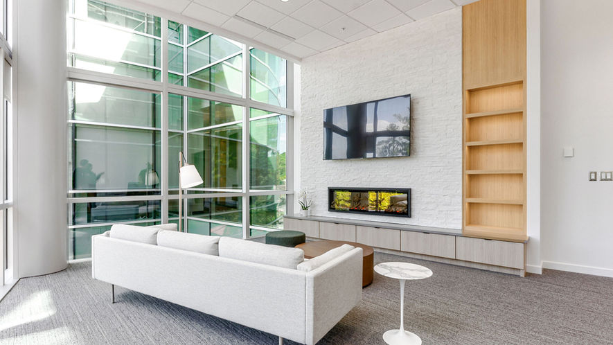 Modern living room with white sofa, TV, and large windows with greenery views.
