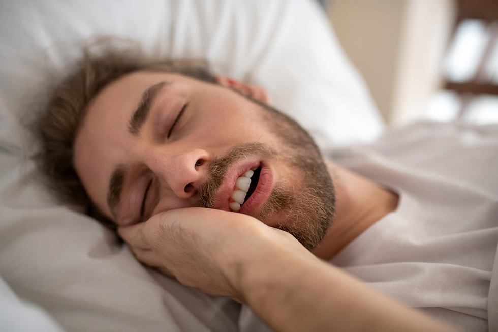 Close-up of a bearded man sleeping on a white pillow, mouth open, in a soft-lit bed.