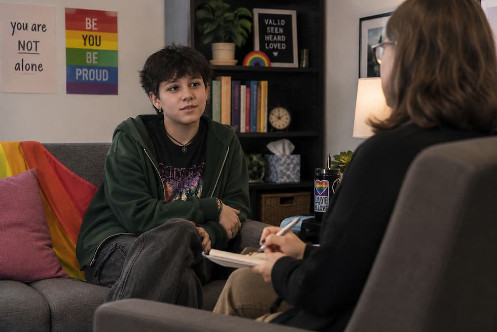 Teen talks with counselor in cozy office with rainbow decor and signs reading You are not alone and Be you be proud.