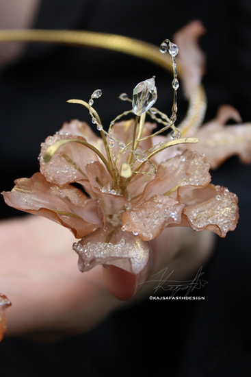 An exquisite high-fashion close-up photograph of a detailed hand-sculpted flower statement jewel in shimmering pearlescent pink and bronze gold tones, designed by Luxembourg Art Prize competitor Kajsa Fasth Design.