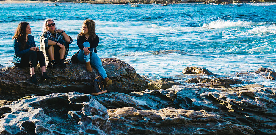 Thre women sitting on a rock on the beach talking