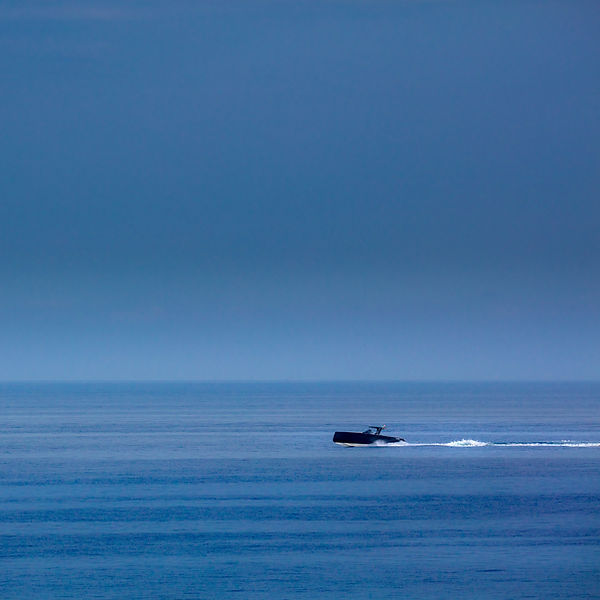 a black small boat running full speed in a very dark blue sea