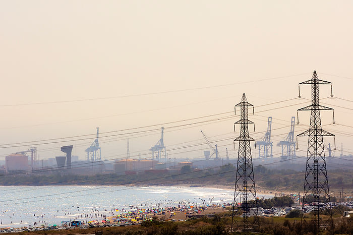 A crowed beach in the middle of an industrial zone