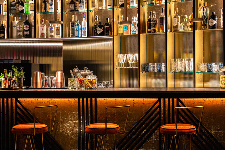 Bar moderno con taburetes rojos, estantes iluminados y botellas de licor.