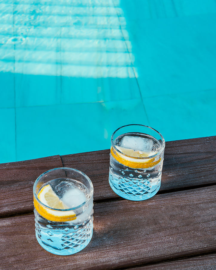 Dos vasos de agua fría con limón y hielo junto a piscina azul.