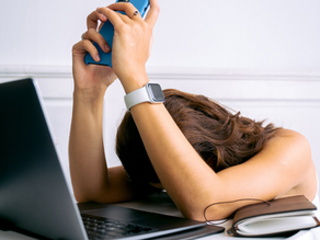 Eine verzweifelte Frau vor dem Laptop mit einem Smartphone in der Hand