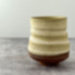Handmade ceramic yunomi-style tea cup with a softly ridged swirl form and trimmed foot, shown on a textured gray surface.