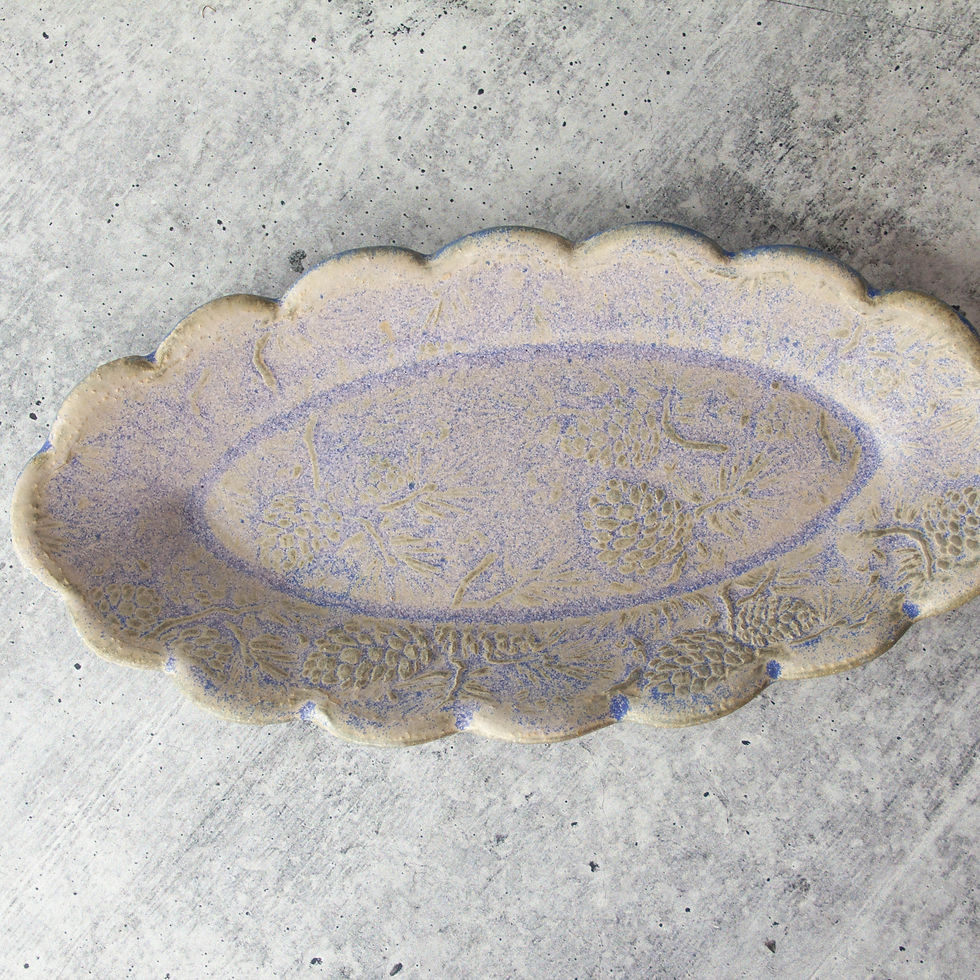 handmade oval ceramic butter dish with scalloped edge and embossed pine cone pattern.