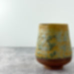 Handmade ceramic yunomi-style tea cup with a smooth curved profile and trimmed foot, shown on a textured gray surface.