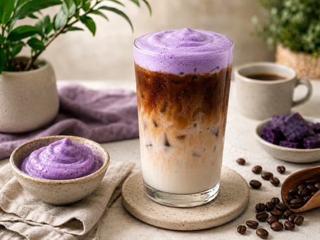 A layered iced ube macchiato in a tall glass featuring cold milk on the bottom, a dark layer of espresso in the center, and a thick, vibrant purple ube cold foam on top next to a small bowl of ube paste.