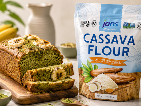 Cassava flour bag beside sliced green banana loaf on a wooden board, with bananas and kitchen props in a bright, natural scene