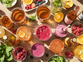 A vibrant top-down view of various colorful functional beverages in glass jars, garnished with fresh fruits like oranges, raspberries, and mint leaves on a wooden table.