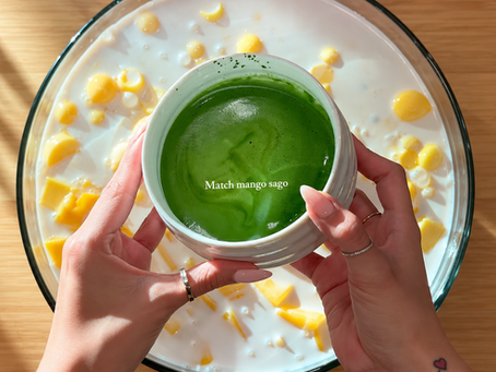 Hands holding a bowl of green matcha mango sago over mango pieces in milk on a wooden table, sunlit and fresh.