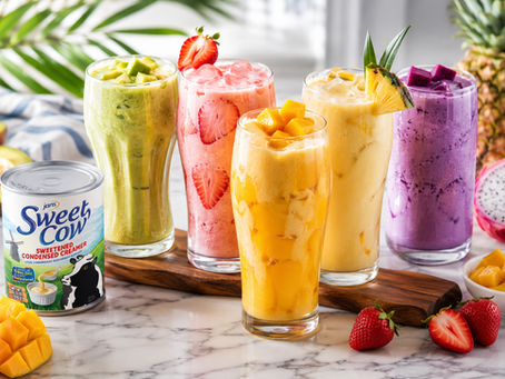 A lineup of four vibrant, colorful fruit smoothies avocado green, strawberry pink, mango yellow, and dragon fruit purple, served in tall glasses next to a can of Jans Sweet Cow Sweetened Condensed Creamer.
