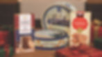 A festive holiday display featuring various Jans products: Danish Legacy Butter Cookies tins, The Royal Danish Butter Cookies, and Tradition Cookie Thins Cinnamon box, surrounded by Christmas gifts.
