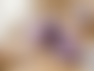 A tiered lavender-colored ube cake decorated with white chocolate curls and flowers, displayed next to a can of Sweet Cow Ube Sweetened Condensed Milk and Easter eggs.