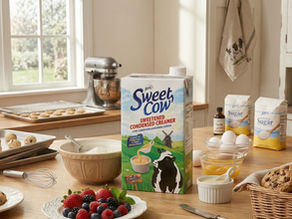 A cozy kitchen scene with Sweet Cow creamer, cookies, berries, and baking ingredients on a wooden counter.
