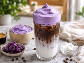 A glass of iced coffee topped with a thick, beautifully dolloped swirl of purple ube coconut cream cold foam, surrounded by an espresso shot, a bowl of ube halaya, and coconut chunks.