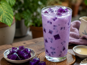 A tall glass filled with a creamy, vibrant purple ube milk drink and translucent dark purple jelly cubes, served over ice on a rustic wooden tabletop next to a small dish of extra jelly.