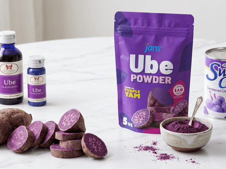 A collection of ube products on a white surface, including sliced fresh purple yams, ube flavoring bottles, a bag of Jans Ube Powder, and a can of Sweet Cow Ube Condensed Milk.