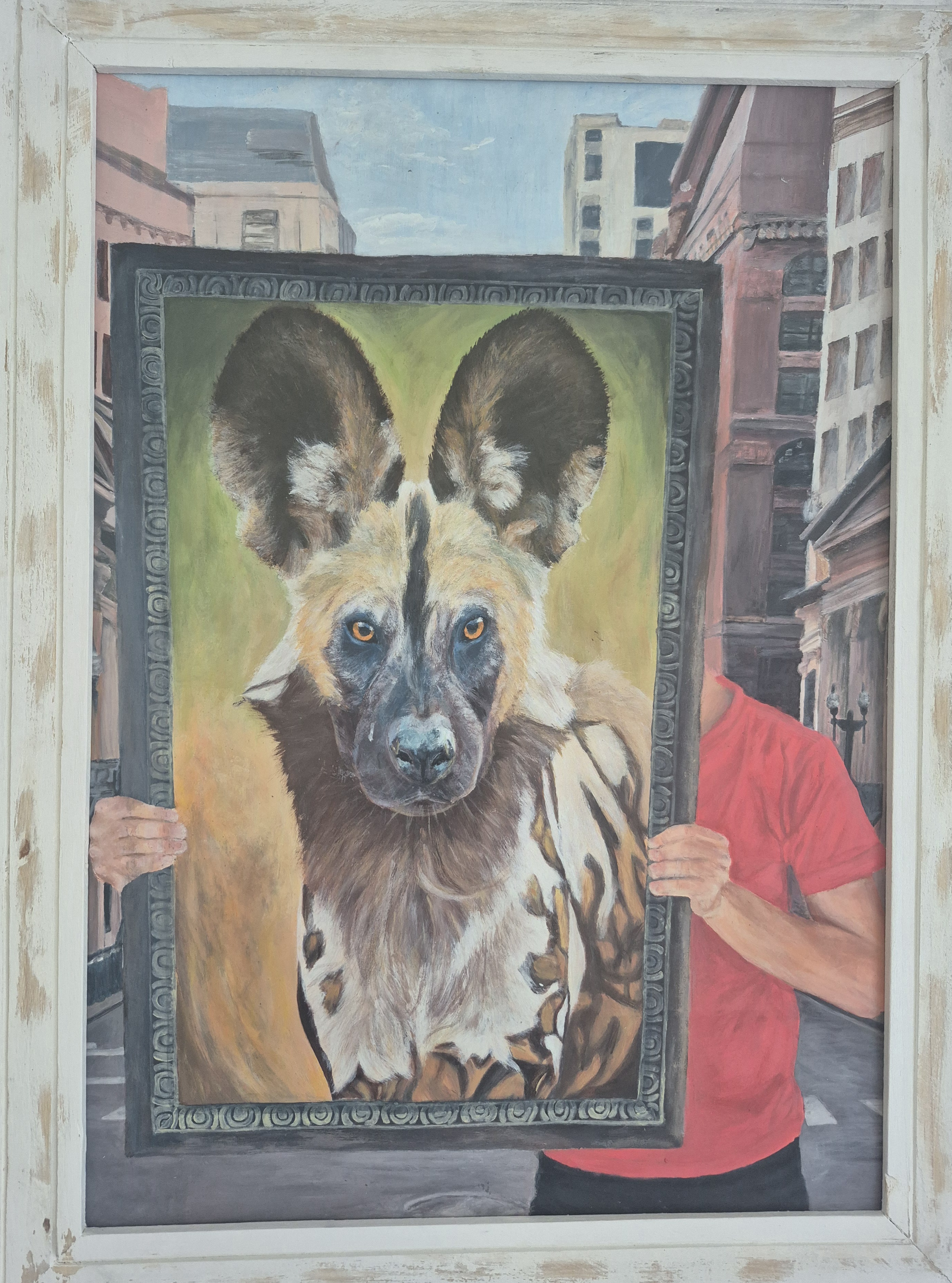 Wild heart in the city by Anuschka de Jager, person holding a framed portrait of an African wild dog against a cityscape
