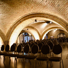 Historischer Eventraum mit Backsteingewölbedecke und Reihen leerer Stühle.