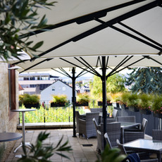 Restaurantterrasse mit Sonnenschirmen, Tischen, Stühlen und Blick auf Weinberge.