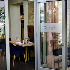 Einladender Restaurant-Eingang mit offenen Glastüren, Schriftzug Enjoy und Tischen.