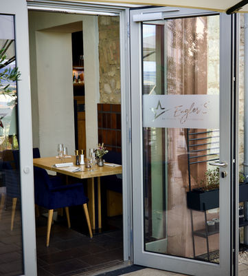 Einladender Restaurant-Eingang mit offenen Glastüren, Schriftzug Enjoy und Tischen.