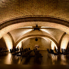 Historischer Gewölbekeller mit warm beleuchteten Ziegelbögen, bereit für eine Veranstaltung.