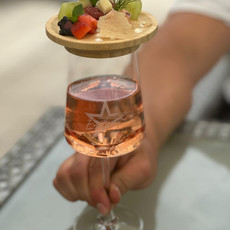 Hand hält Weinglas mit Roséwein, darüber schwebt ein Teller frischer Früchte.