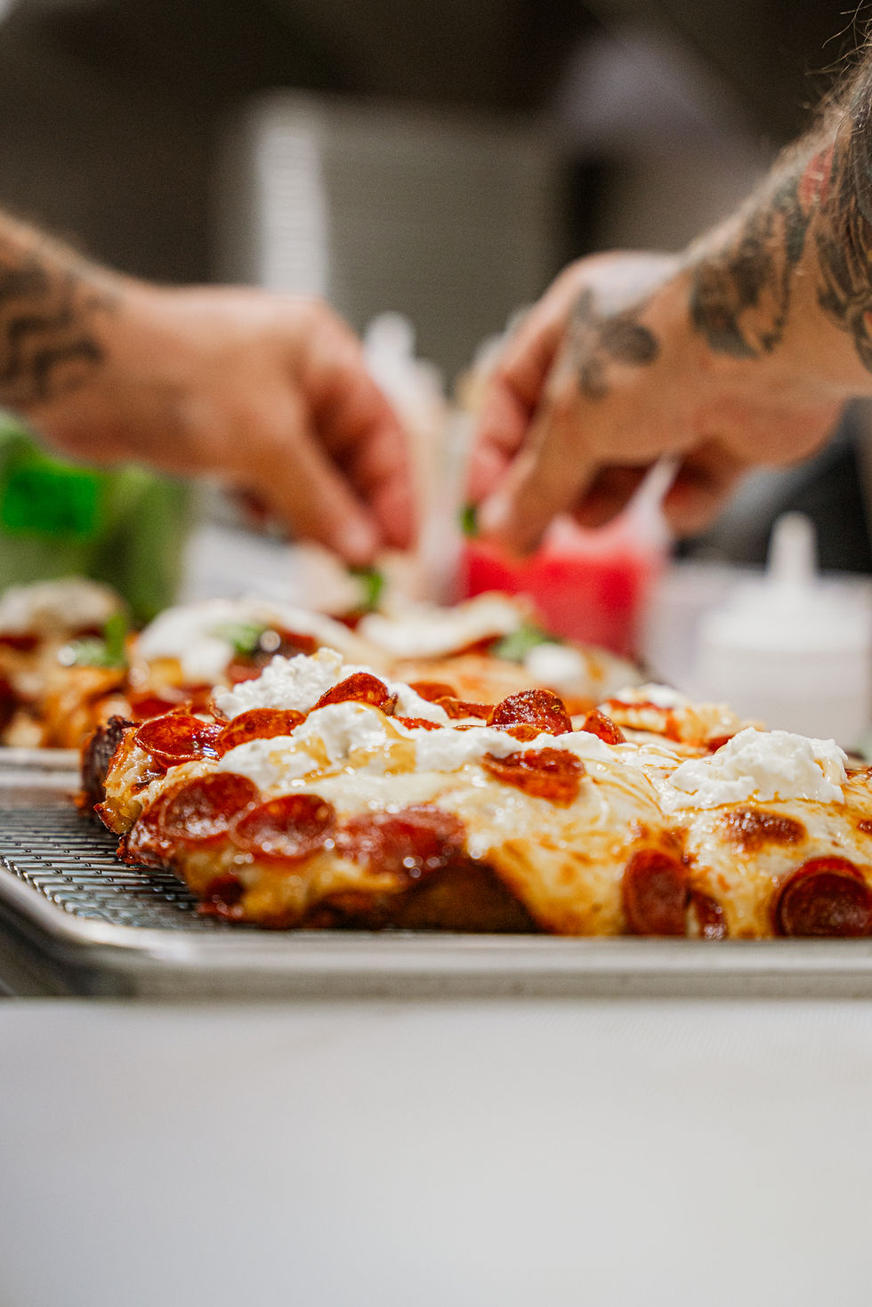 two hands adding ingredients to pizza