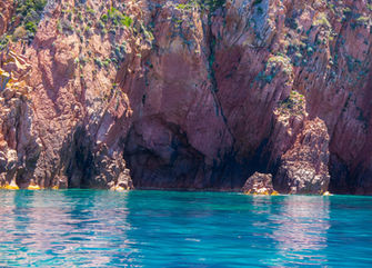 Ingresso di una grotta marina naturale tra rocce rosse e acqua turchese in Corsica