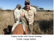 Safari hunter poses with a dead vervet monkey on a termite mound in dry grassland; caption reads Trophy hunter with Vervet monkey.