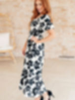 Woman wearing floral print dress, standing with hand on hip near chair.