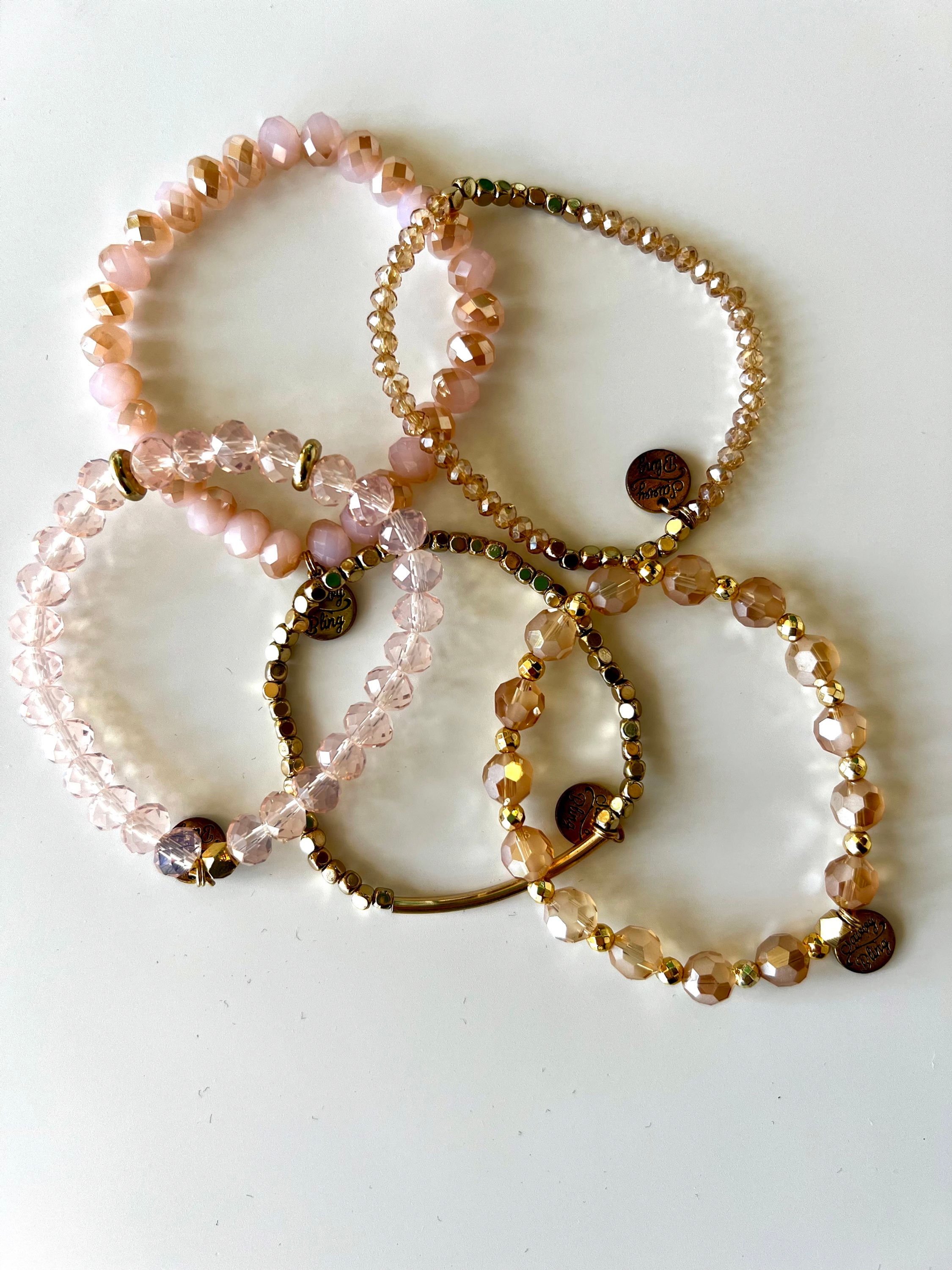 Five beaded bracelets in shades of pink and gold on a white surface