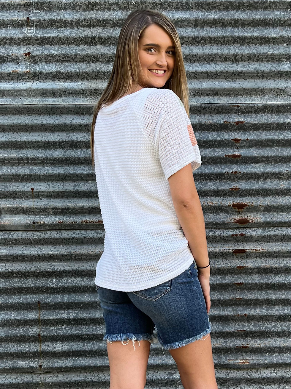 Thumbnail: Woman wearing white top and jean shorts smiling in front of metal wall