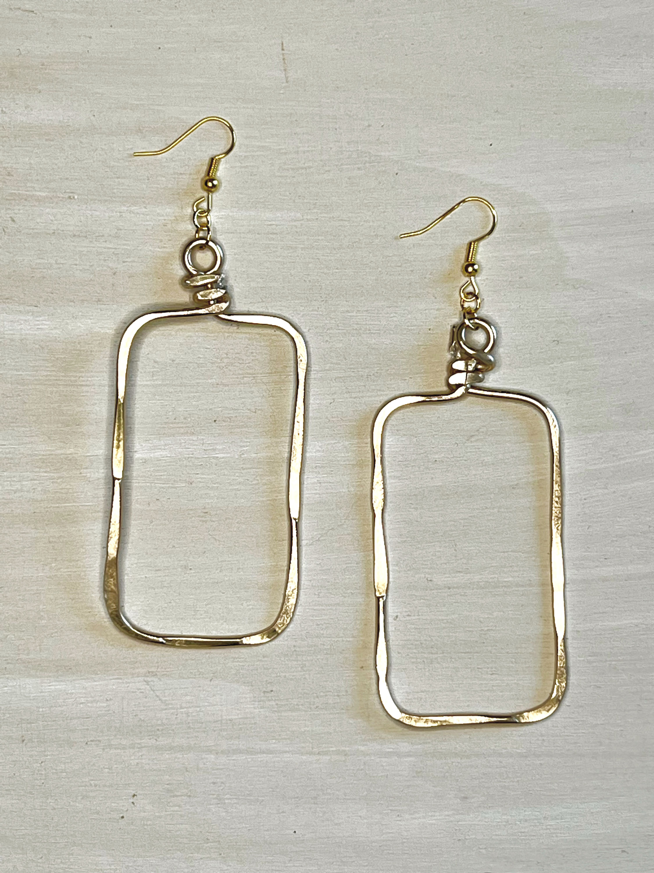 Pair of silver and gold rectangle earrings on a wooden background.