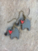 Gray elephant earrings with red hearts displayed on a textured stone background.