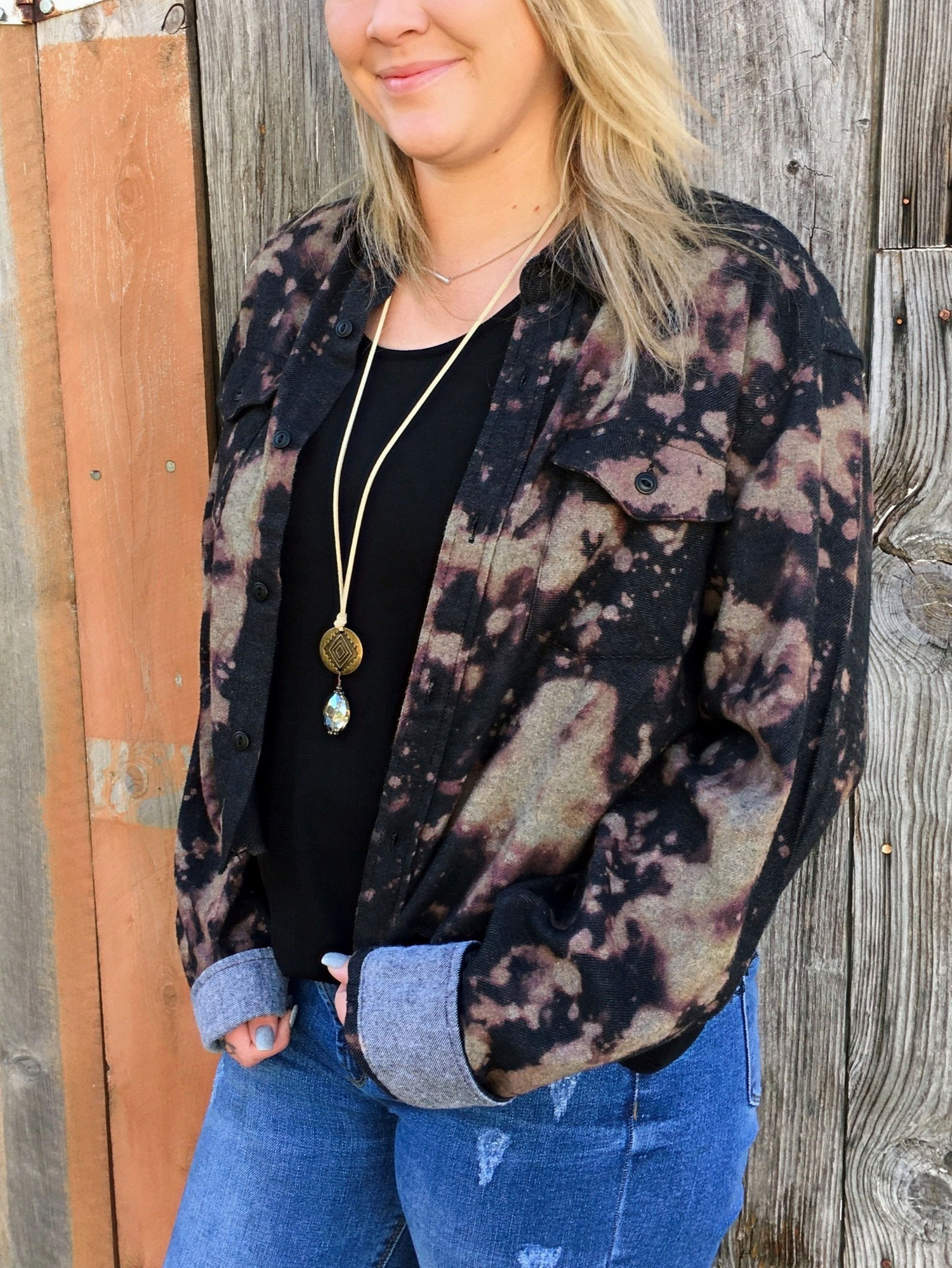Woman wearing black shirt and bleached jacket with long necklace, wood background.