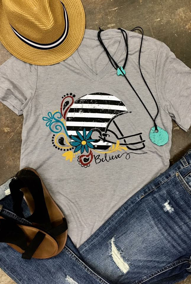 Gray football helmet shirt with Believe text and floral design on display.
