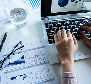 Hands typing on laptop with graphs on desk - Financial Sector Investigative & Consulting for combating all Financial Crimes