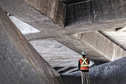 Bauarbeiter mit Sicherheitsweste und Helm inspiziert massive Betonstruktur, beeindruckende Architektur.