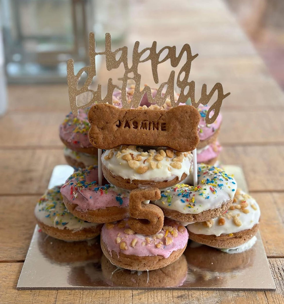 A pink and white doughnut cake, with a custom name bone and age cookie., A "Happy Birthday" cake topper on cake.
