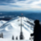 Powder white Mountain with a ski lift behind with two or three skiers in the middle at the