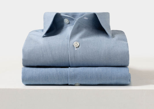 Folded made-to-measure shirts in light blue fabric, showcasing craftsmanship and tailored design, reflecting Allan David Bespoke's commitment to personalized style and comfort.