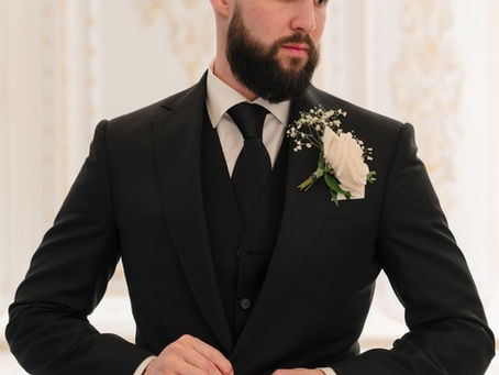 Groom wearing a black bespoke wedding suit with boutonnière, adjusting jacket in an elegant setting.