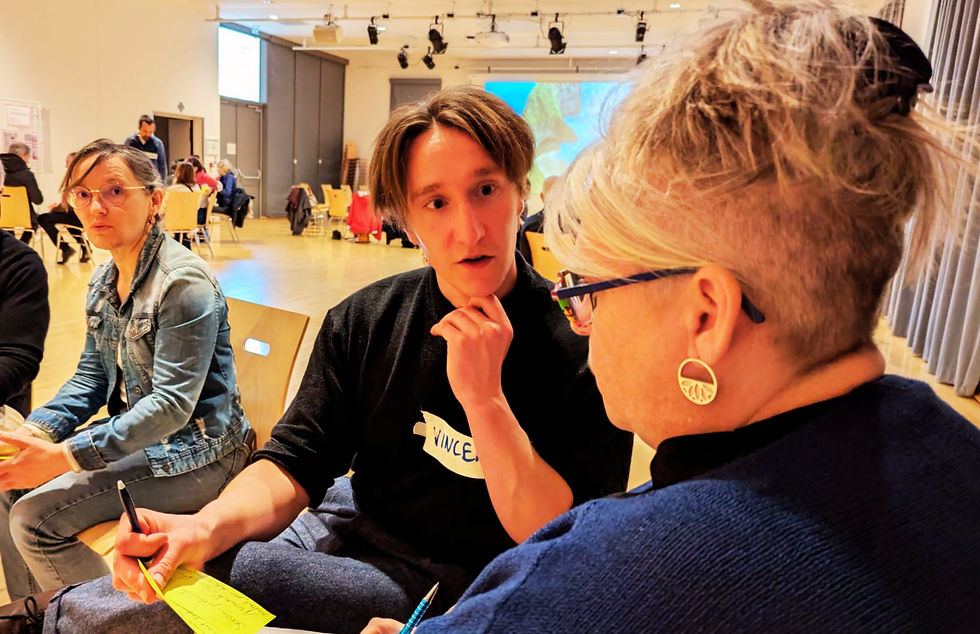 Photographie de quatre personnes, deux femmes et deux hommes, d'âges différents, qui conversent lors d'une assemblée.