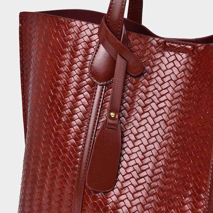 Thumbnail: Detail shot of sturdy shoulder strap and leather charm on a cognac woven work bag