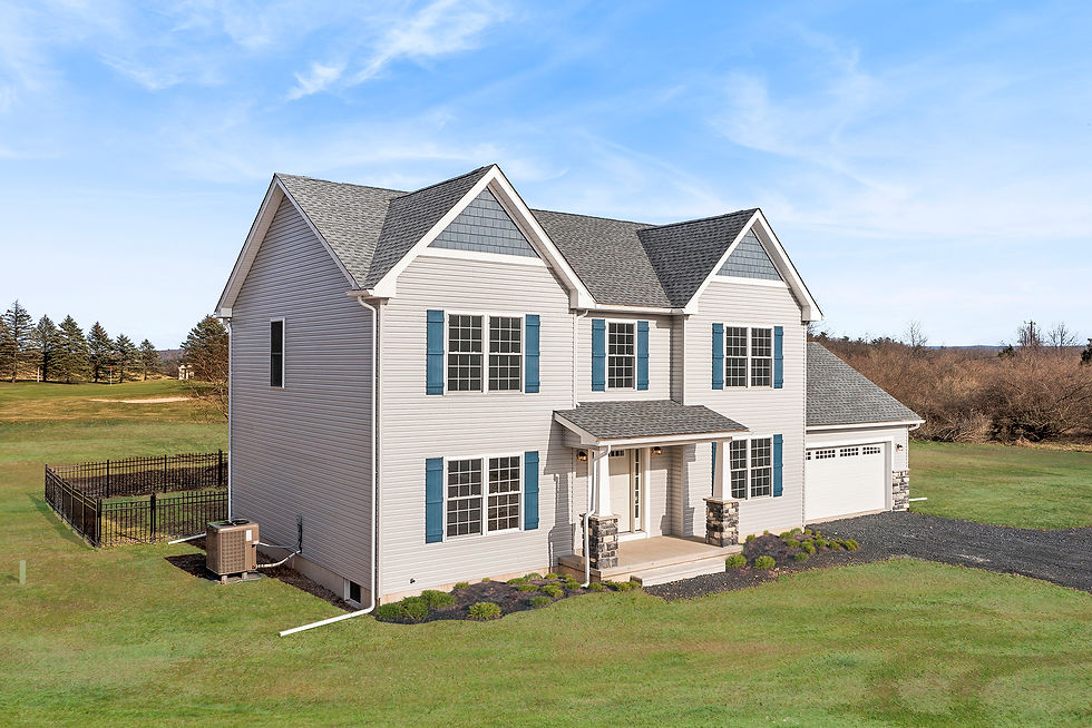 Front-left exterior view of a two-story craftsman style gray vinyl-sided home with blue shutters, a covered front porch with stone columns, and an attached two-car garage on a grassy lot under a clear blue sky.